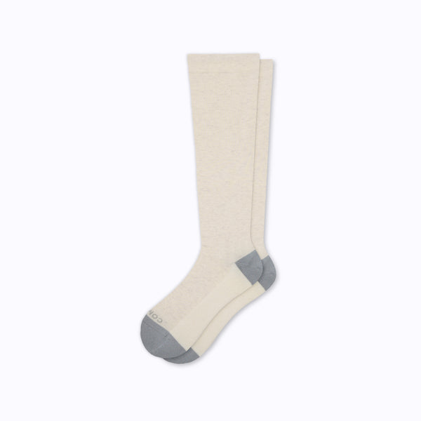 Flat pair of bone colored knee-high socks with grey heel and toe on light grey background