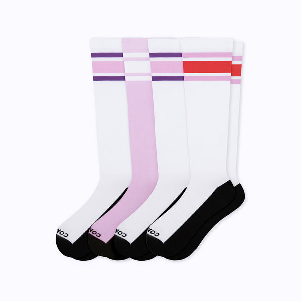 Four pairs of white knee-high socks with black toes and heels, arranged in a fan shape on a light gray background. Each pair has different stripe accents at the top: purple, light pink, and red.
