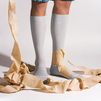 Person wearing gray knee-high socks with a beige ribbon on a light background