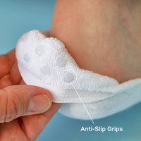 A close-up of a white textured anti-slip sock being held by a hand, with a finger pointing to a raised grip pad and the text 'Anti-Slip Grips' on a light blue background.