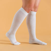 White recycled cotton compression socks on a model on a beige background.