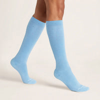 Model wearing light blue knee-high socks with colorful flecks standing on a beige background
