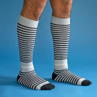 Grey and black stripe knee-high compression socks on a model on a blue background.