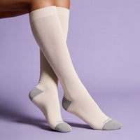 Model sitting with crossed legs wearing bone colored knee-high socks on a purple background