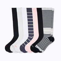Seven pairs of knee-high socks arranged in a fan shape on a light gray background. The socks feature various patterns including solid black, white speckles, navy blue stripes, light pink stripes, and black and white horizontal stripes.
