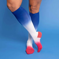 Model wearing blue to white to red ombre knee-high socks standing on a blue background