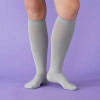 Gray knee-high socks worn by a person on a purple background