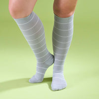 Model wearing grey with white stripe knee-high socks standing on a light green background