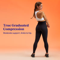 Model wearing black high-waisted leggings in a white sports bra standing on an orange ombre background. Text overlay True Graduated Compression, Moderate support. Ankle to hip.