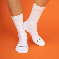 Close-up image of person standing wearing white crew length socks on a bright orange backdrop