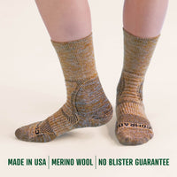 Pair of brown and gray patterned socks on a white background with text about merino wool and a guarantee.