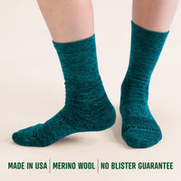 Teal socks worn by a person on a beige background with text about merino wool and product guarantees.