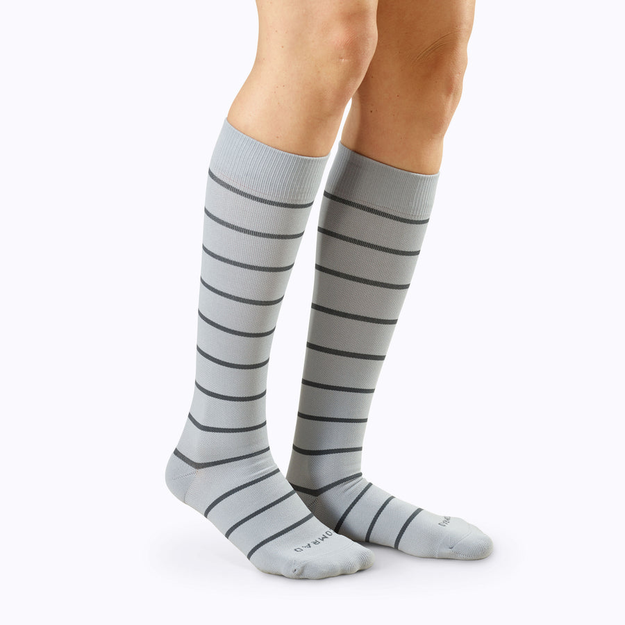 Side view of legs wearing a pair of knee high compression socks in grey-charcoal stripes
