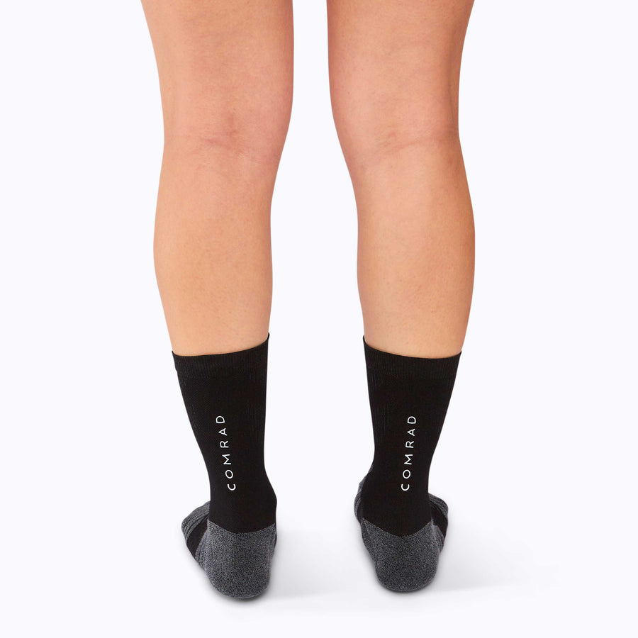 Back view of a pair of legs wearing an athletic crew compression socks black solid
