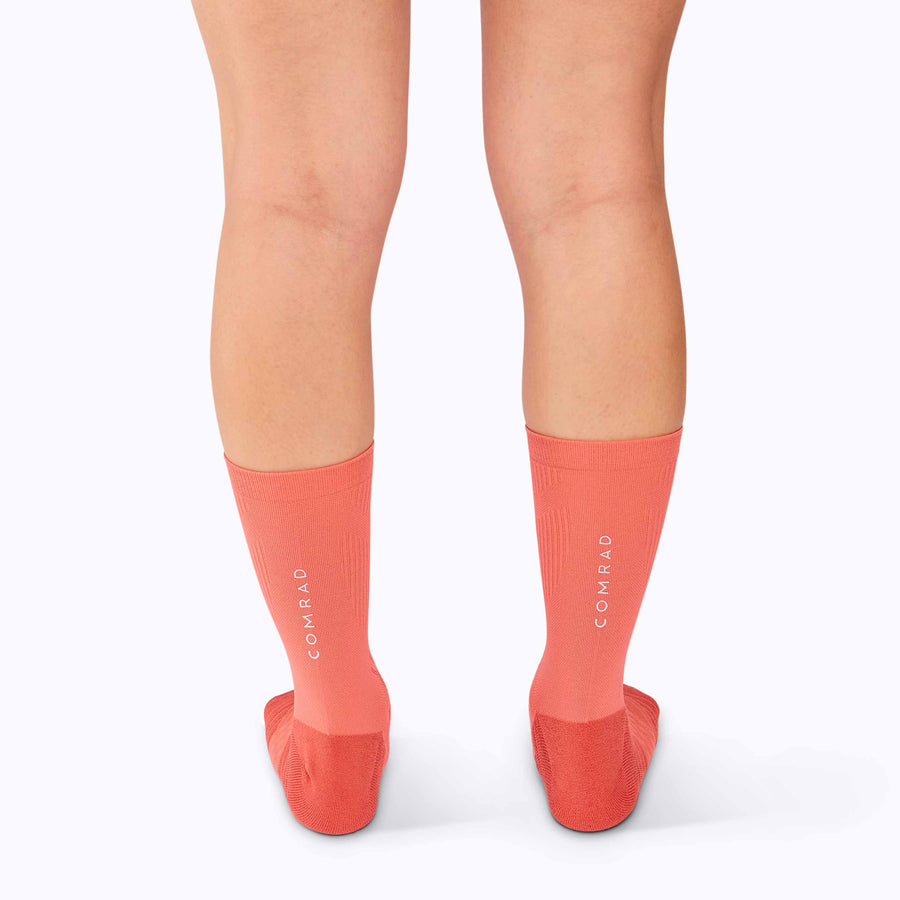 Back view of a pair of legs wearing an athletic crew compression socks coral solid