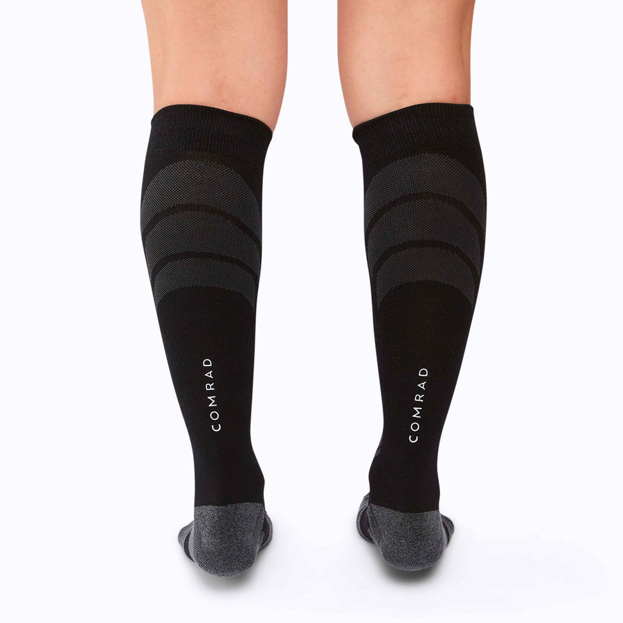 Back view of feet wearing an athletic knee high performance blend socks black solid