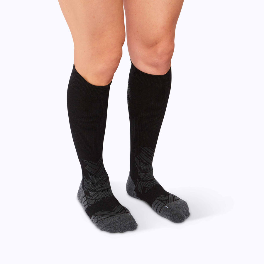 Side view of feet wearing an athletic knee high performance blend socks black solid