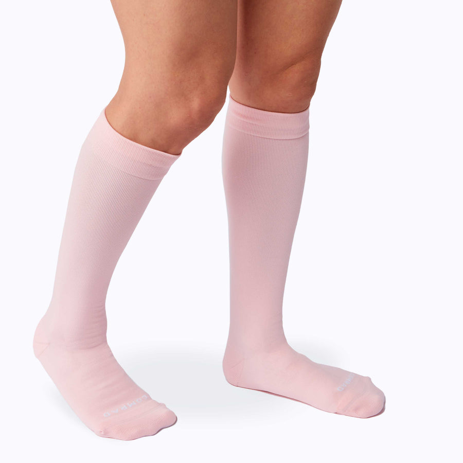 Side view of a pair of legs wearing nylon knee high compression socks in rose solid