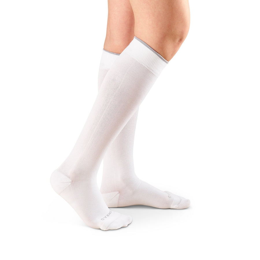 Side view of a pair of legs wearing nylon knee high compression socks in white solid