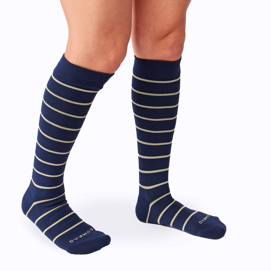 Side view of a pair of legs wearing nylon knee high compression socks in navy-sand stripes