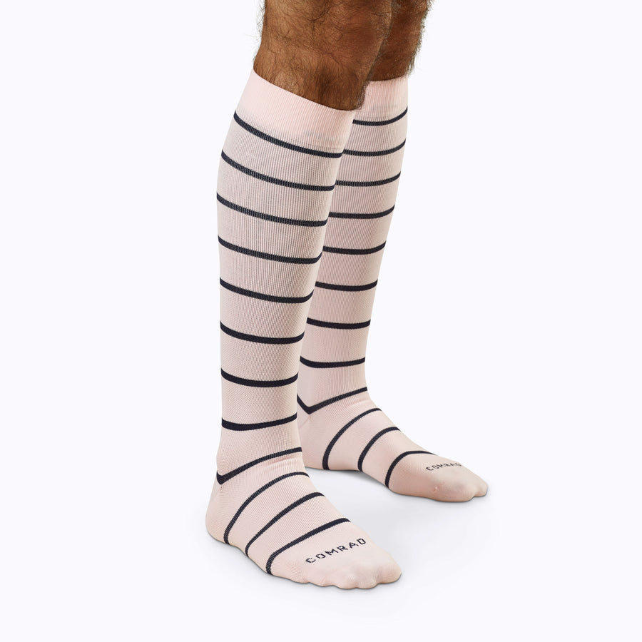 Side view of a pair of legs wearing nylon knee high compression socks in rose-navy stripes