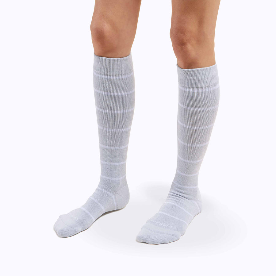 Side view of a pair of legs wearing nylon knee high compression socks in heather-white stripes